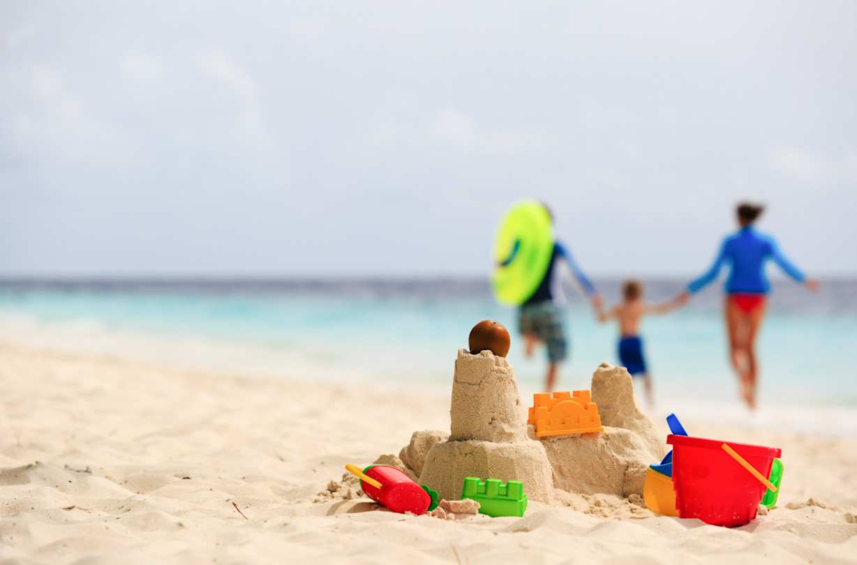 A close up view of a sandcastle and some beach toys in front of a young family in the background at the beach
