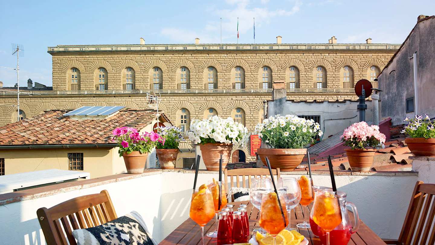 An outdoor table with glasses of Aperol Spritzes facing the Palazzo Pitti, Plum Guide home Alberata Selva in Florence, Italy