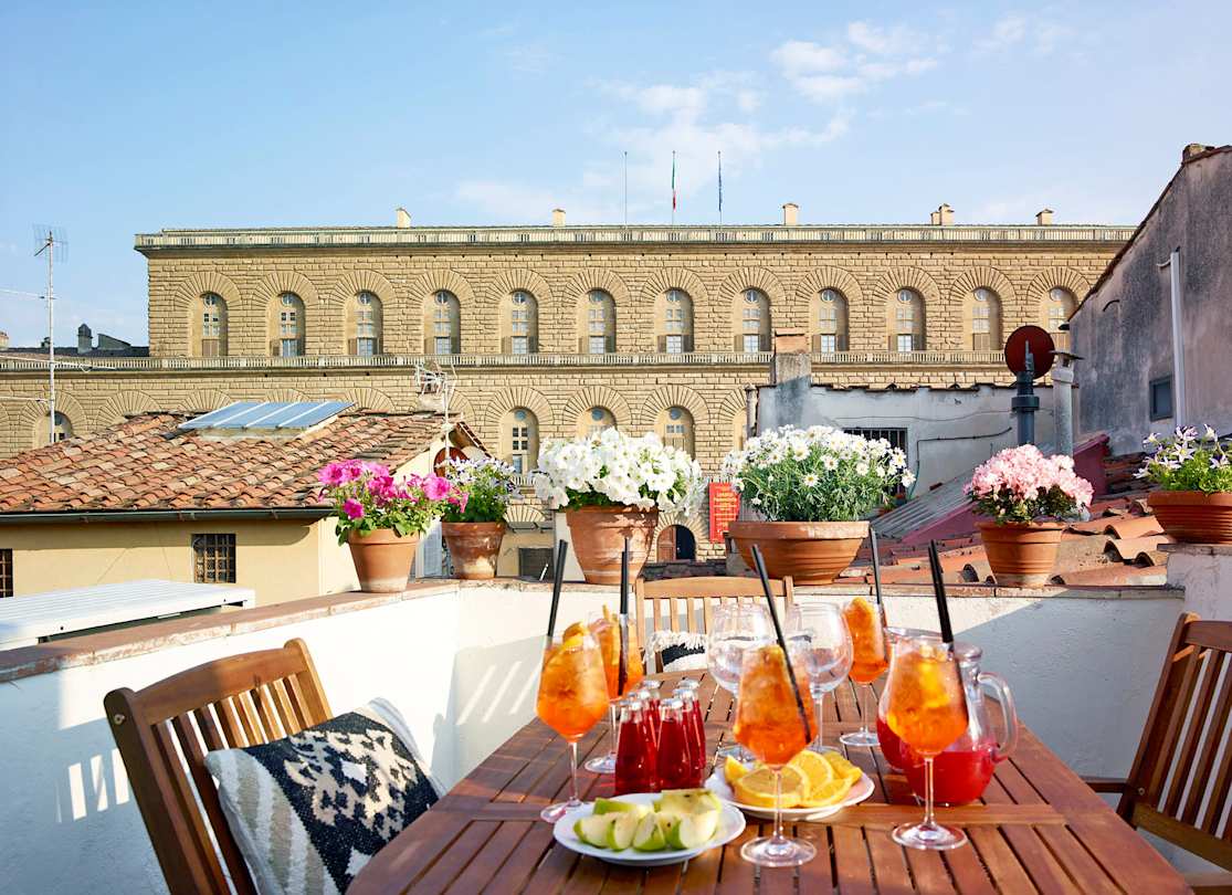 An outdoor table with glasses of Aperol Spritzes facing the Palazzo Pitti, Plum Guide home Alberata Selva in Florence, Italy