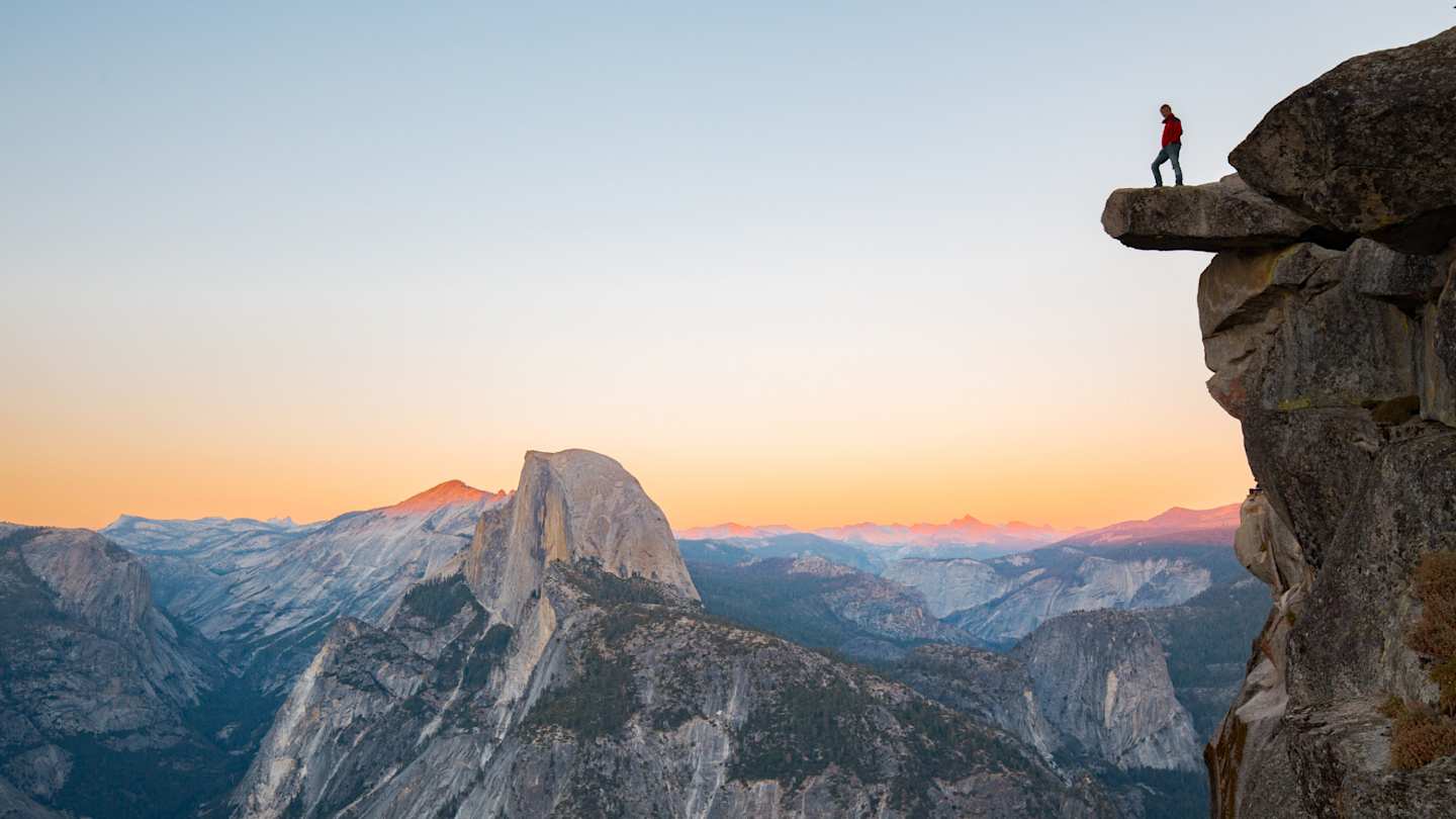 A hiker standing on a tall rock over Half Dome at sunset, Yosemite National Park, USA