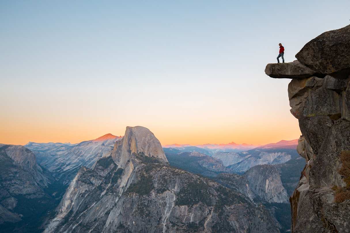 A hiker standing on a tall rock over Half Dome at sunset, Yosemite National Park, USA