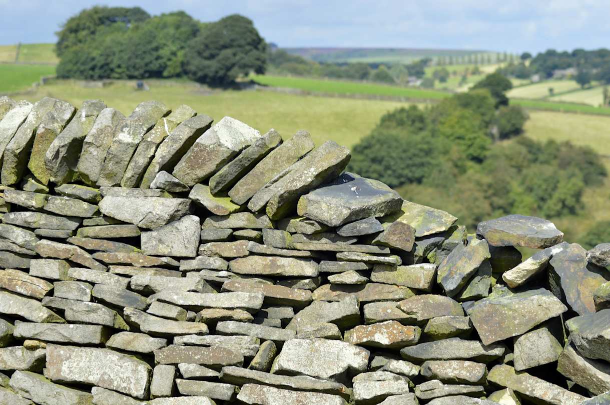 Close up of a grey dry stone wall in front of green fields in Derbyshire, England, UK