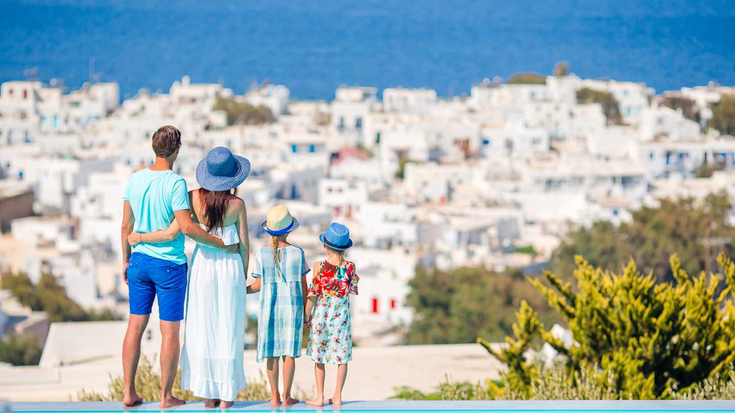 A young family standing by a pool looking over the Greek island