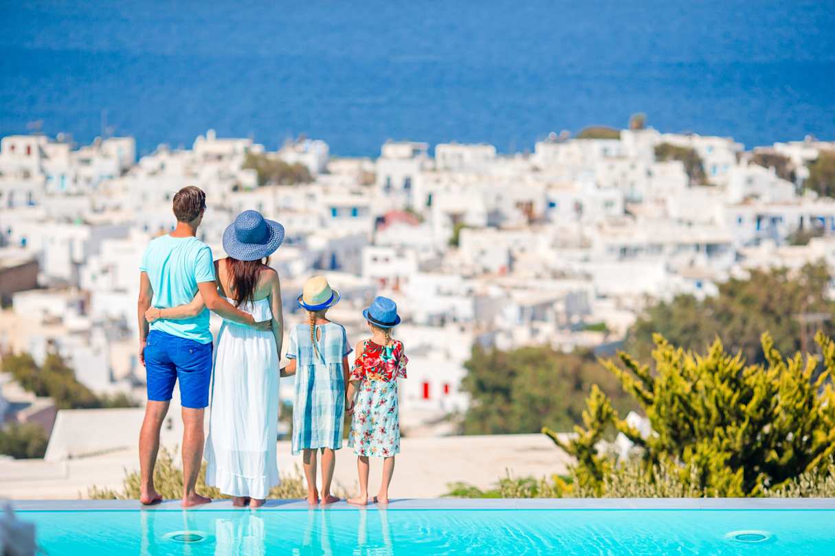 A young family standing by a pool looking over the Greek island