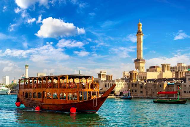 An old wooden ship and Grand Bur Dubai Masjid Mosque on the bay Creek in Deira, Dubai, UAE