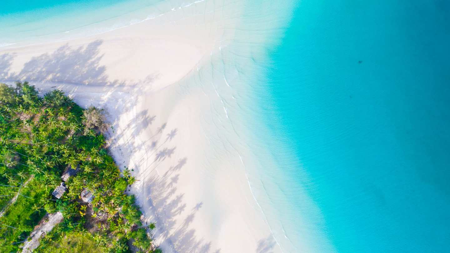 A bird's eye view of white sand and crystalline blue water by green trees at a beach in Mauritius