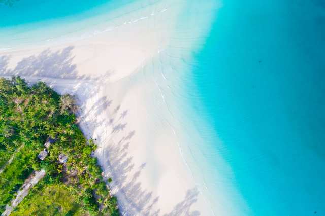 A bird's eye view of white sand and crystalline blue water by green trees at a beach in Mauritius