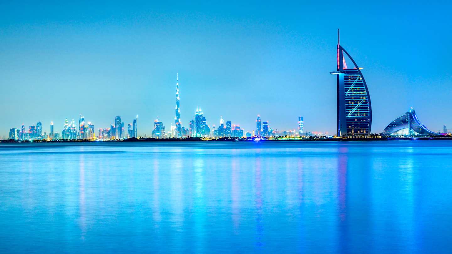A view of the city skyline from across the sea against a blue sky at night, Dubai, UAE