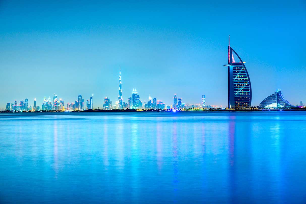 A view of the city skyline from across the sea against a blue sky at night, Dubai, UAE
