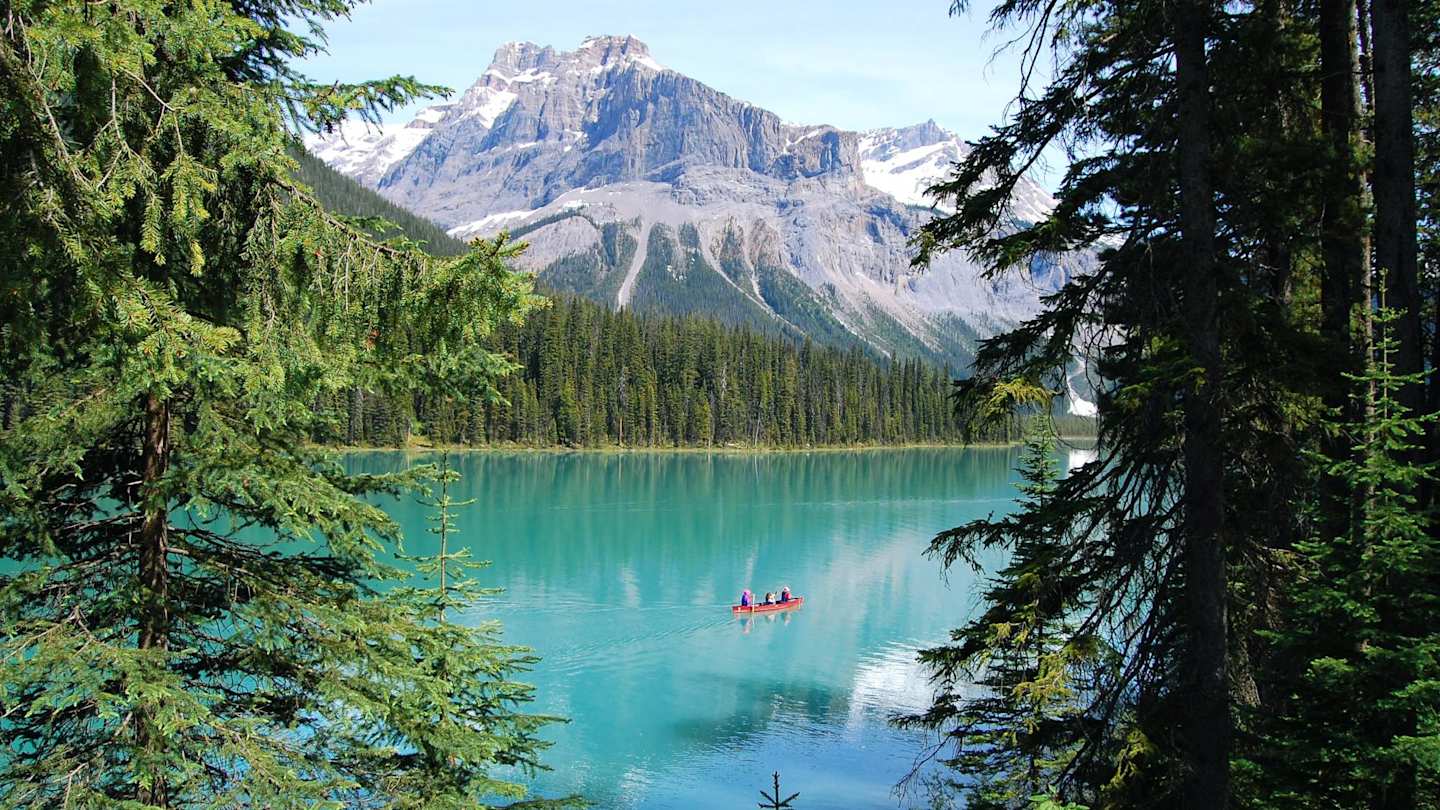 People in a red kayak on the turquoise Emerald Lake in front of green trees and snow-capped mountains, Canada