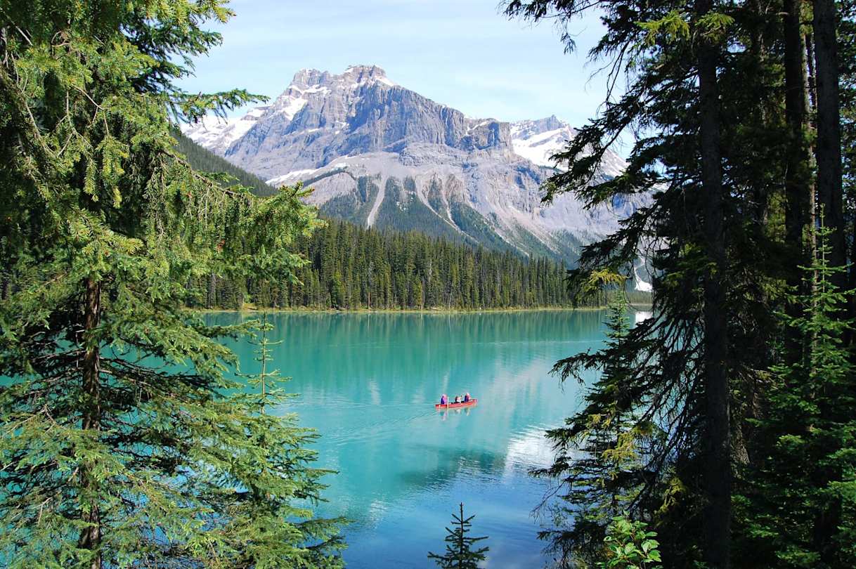 People in a red kayak on the turquoise Emerald Lake in front of green trees and snow-capped mountains, Canada