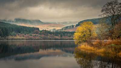 A still lake in front of trees and mountains at Brecon Beacons, Wales, UK