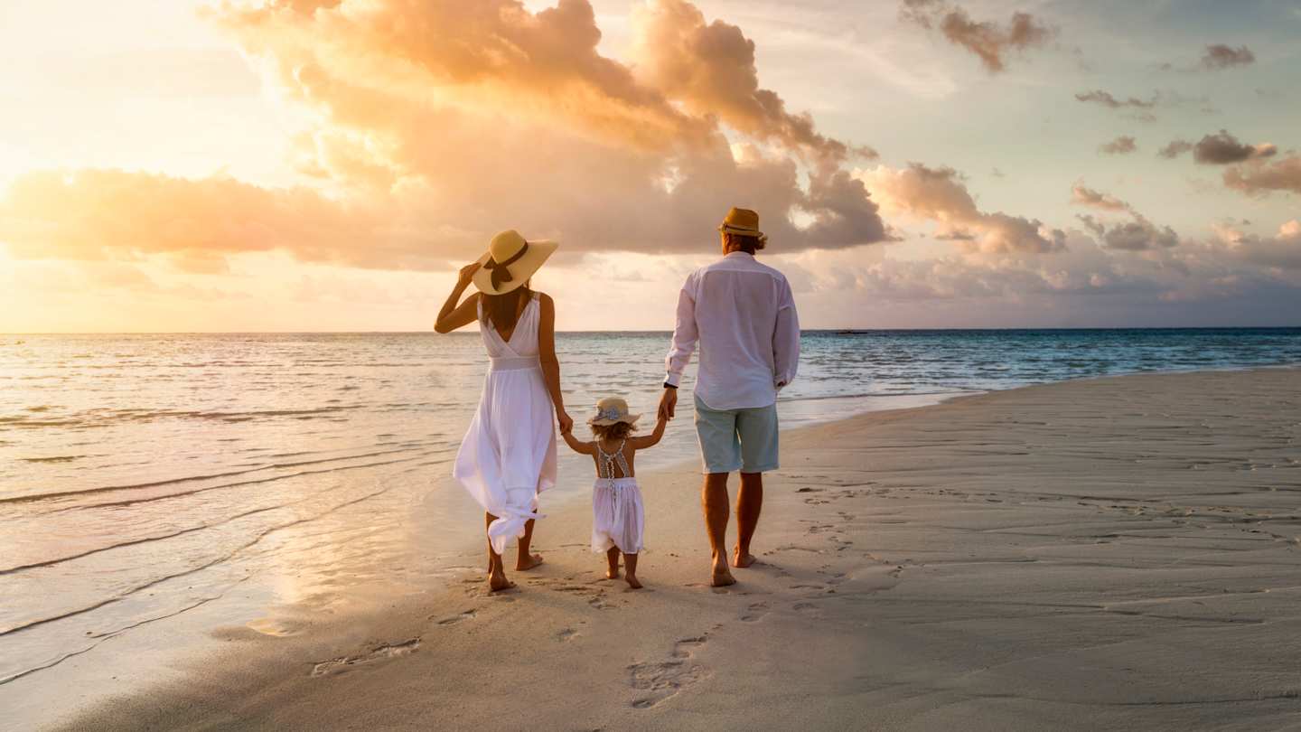 A young family walking along the beach at sunset