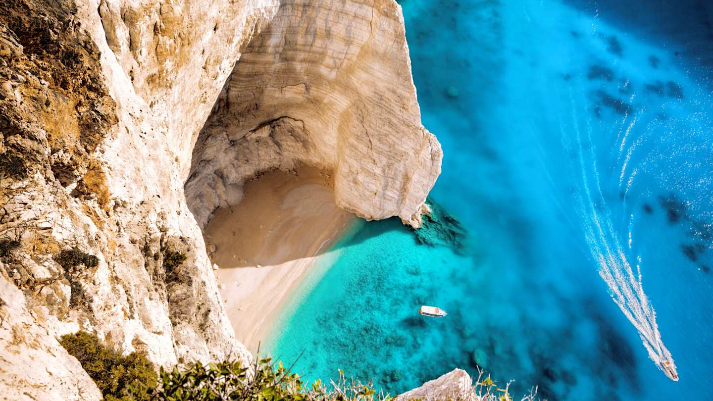 A bird's eye view of a white boat on the clear blue sea by a beach in Zakynthos, Greece