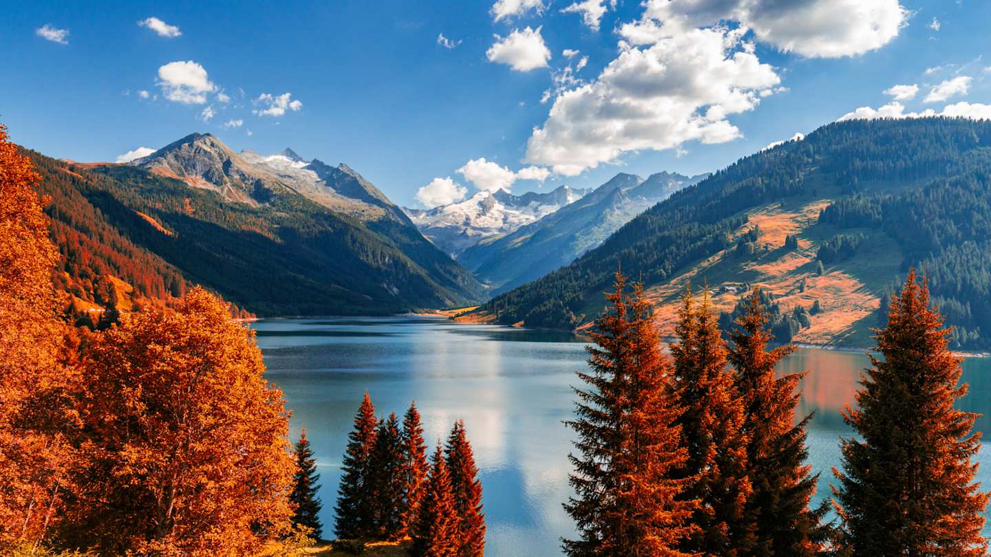 Red and orange trees in front of a large lake and mountains in Tyrol, Austria