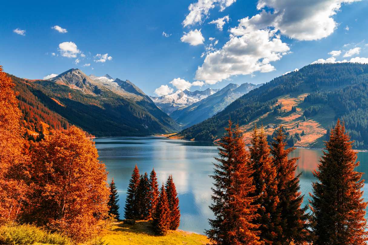 Red and orange trees in front of a large lake and mountains in Tyrol, Austria
