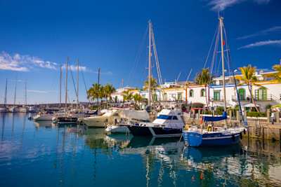 Traditional fishing boats bobbing in the Marina of Puerto de Mogan in front of a palm-lined promenade, Gran Canaria