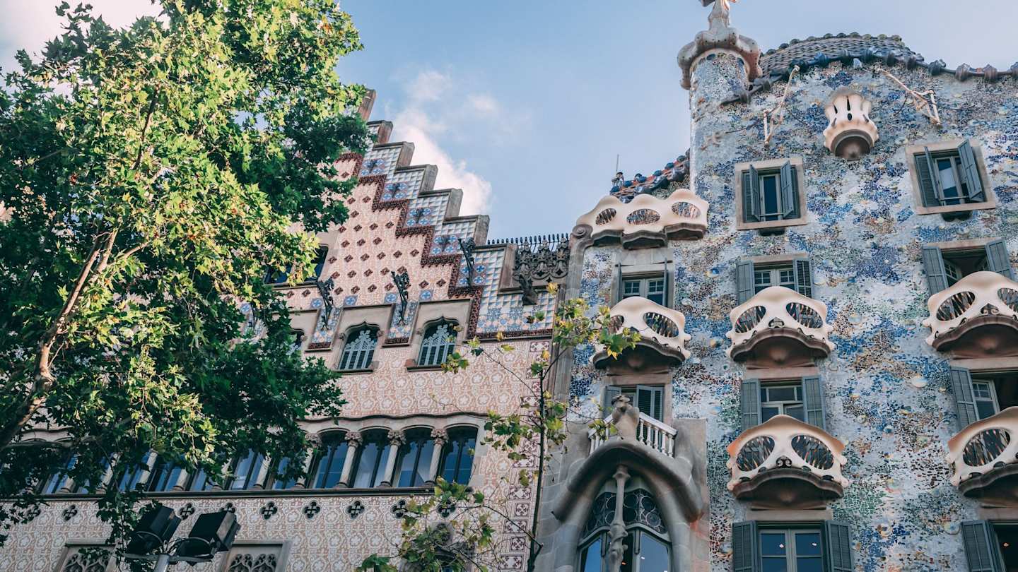 The Gaudí masterpiece Casa Batlló and a tiled building on a tree-lined street in Barcelona, Spain
