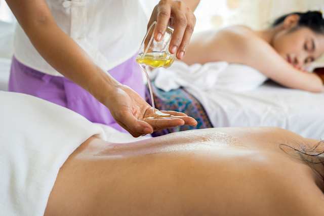 A masseuse pouring oil on her hand in by a client in a spa
