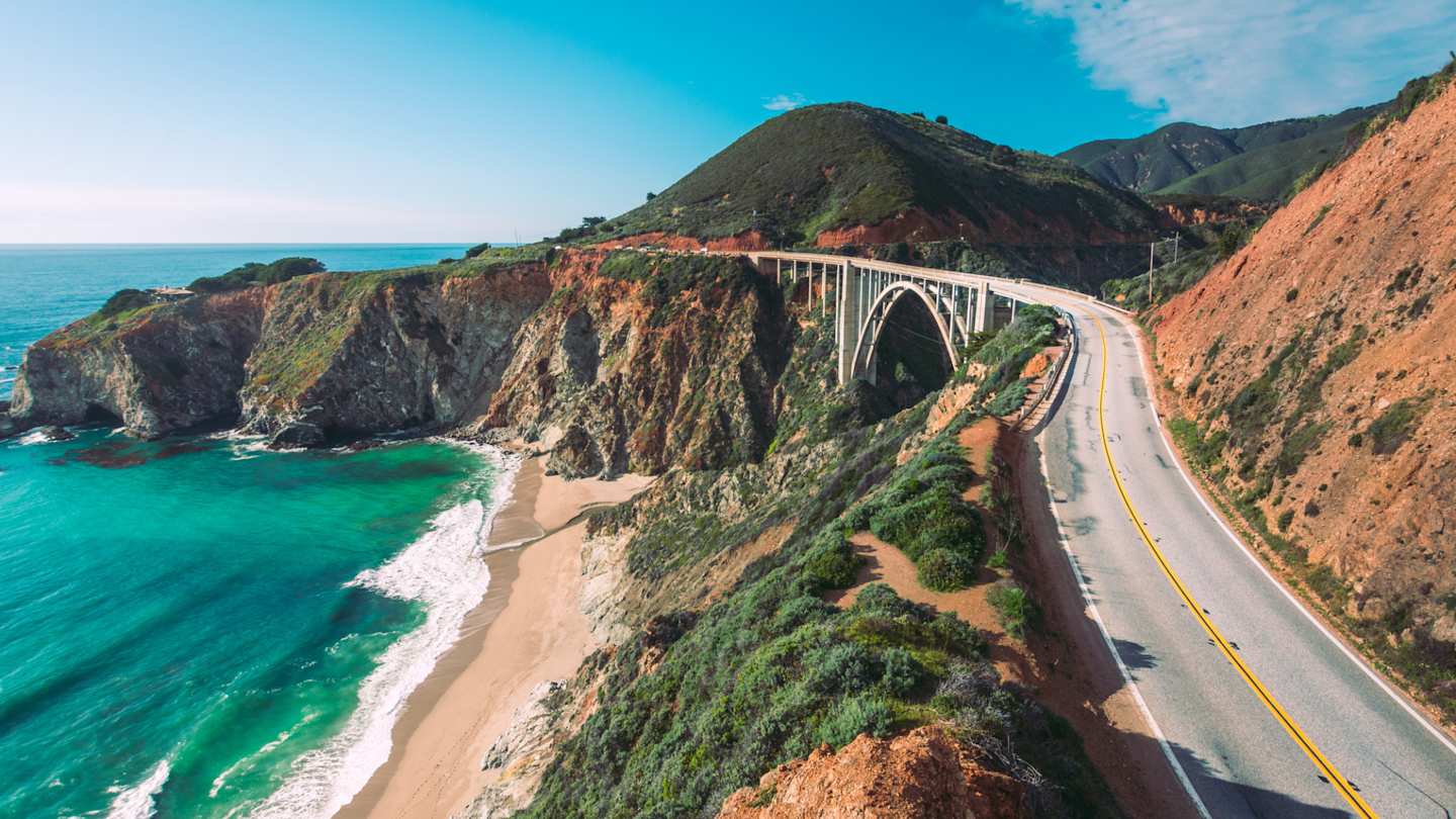 The Pacific Coast Highway, alongside the bright blue sea and tall hills, California, US