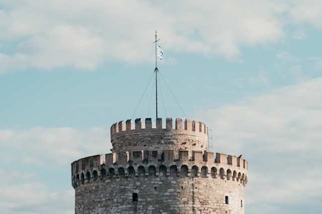 The top of the White Tower of Thessaloniki, with a Greek flag waving against a blue sky, Thessaloniki, Greece