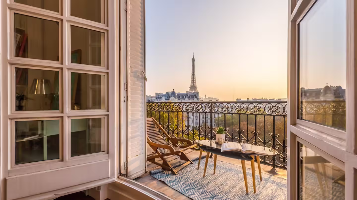 Wooden deck chair and wrought-iron balcony at sunset, a view of the Eiffel Tower in the distance, Paris
