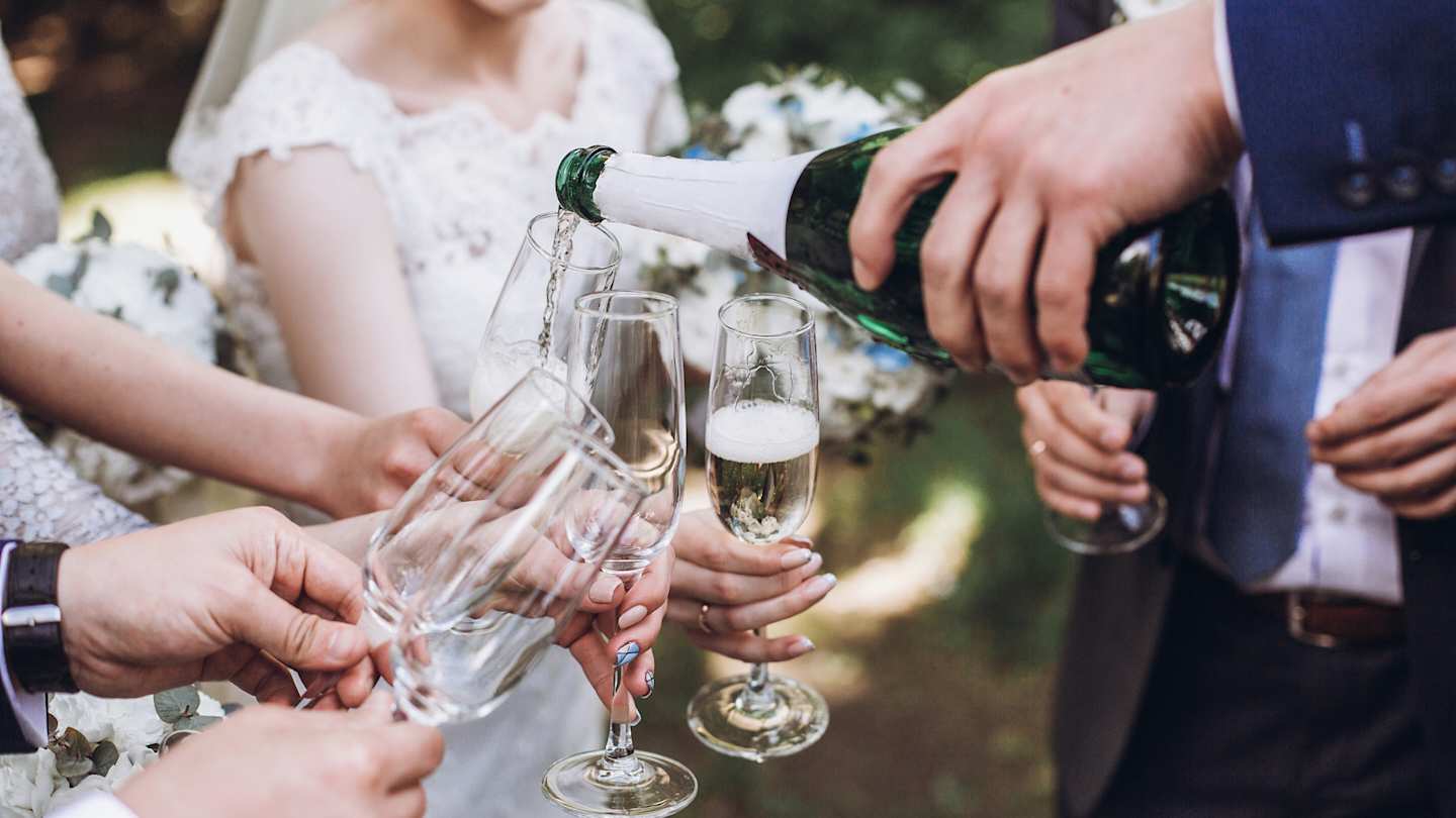 Happy group of people, including a bride and groom, toasting with champagne after a wedding