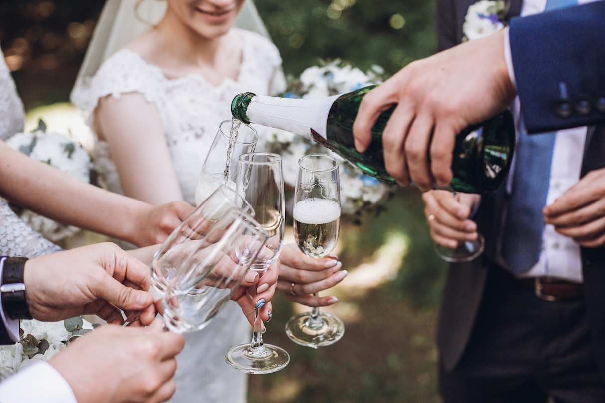 Happy group of people, including a bride and groom, toasting with champagne after a wedding
