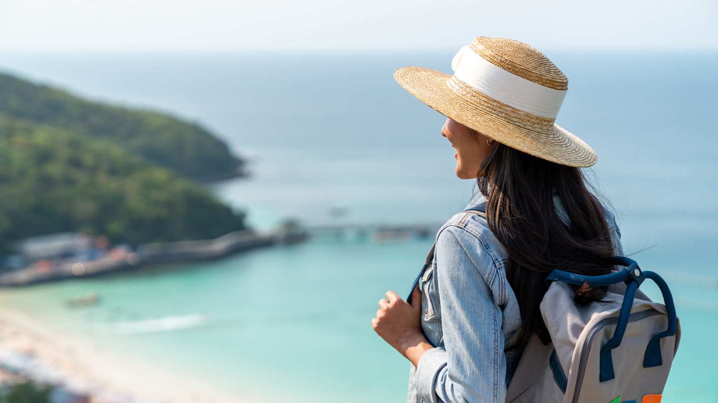 A young woman smiling as she walks near a sandy beach on holiday