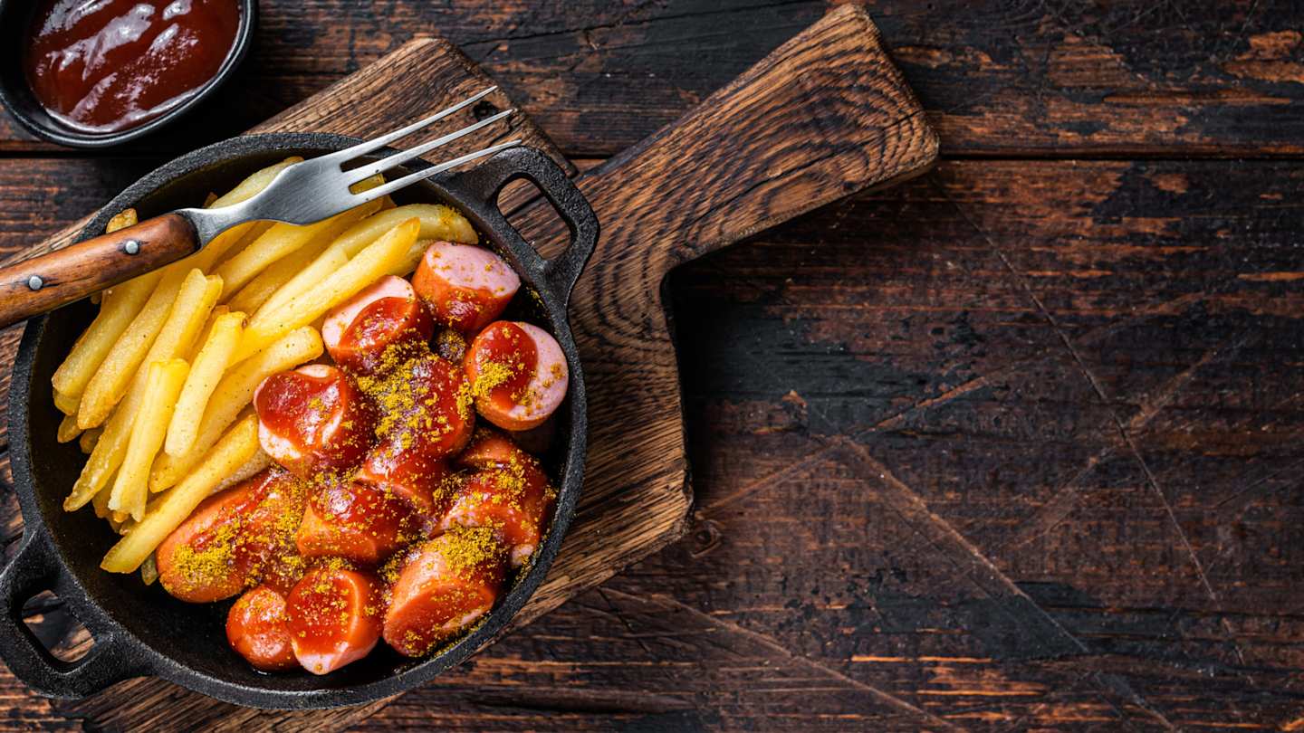 A bird's eye view of currywurst and french fries on a wooden table in Berlin, Germany