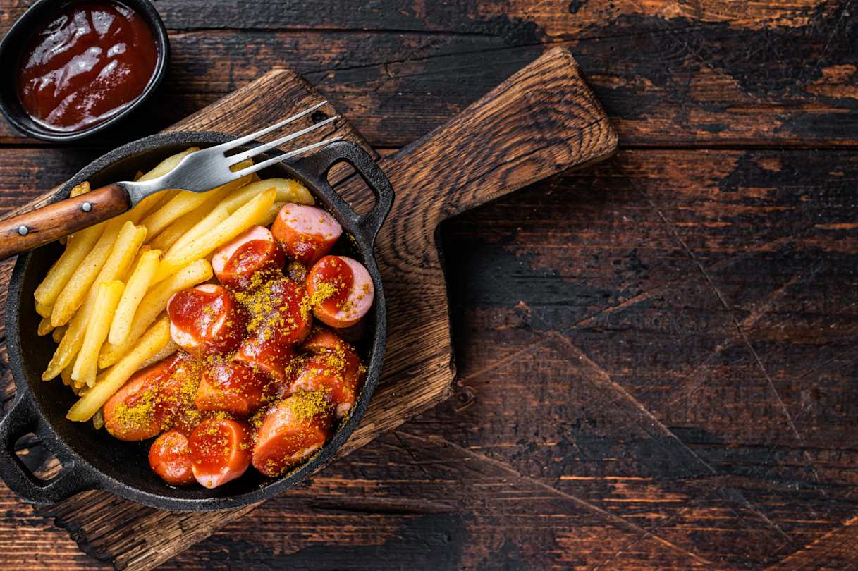 A bird's eye view of currywurst and french fries on a wooden table in Berlin, Germany
