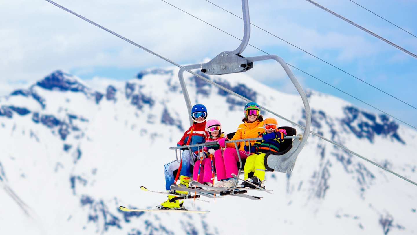 A family wearing colourful clothes on a ski lift at a ski resort in front of snowy mountains