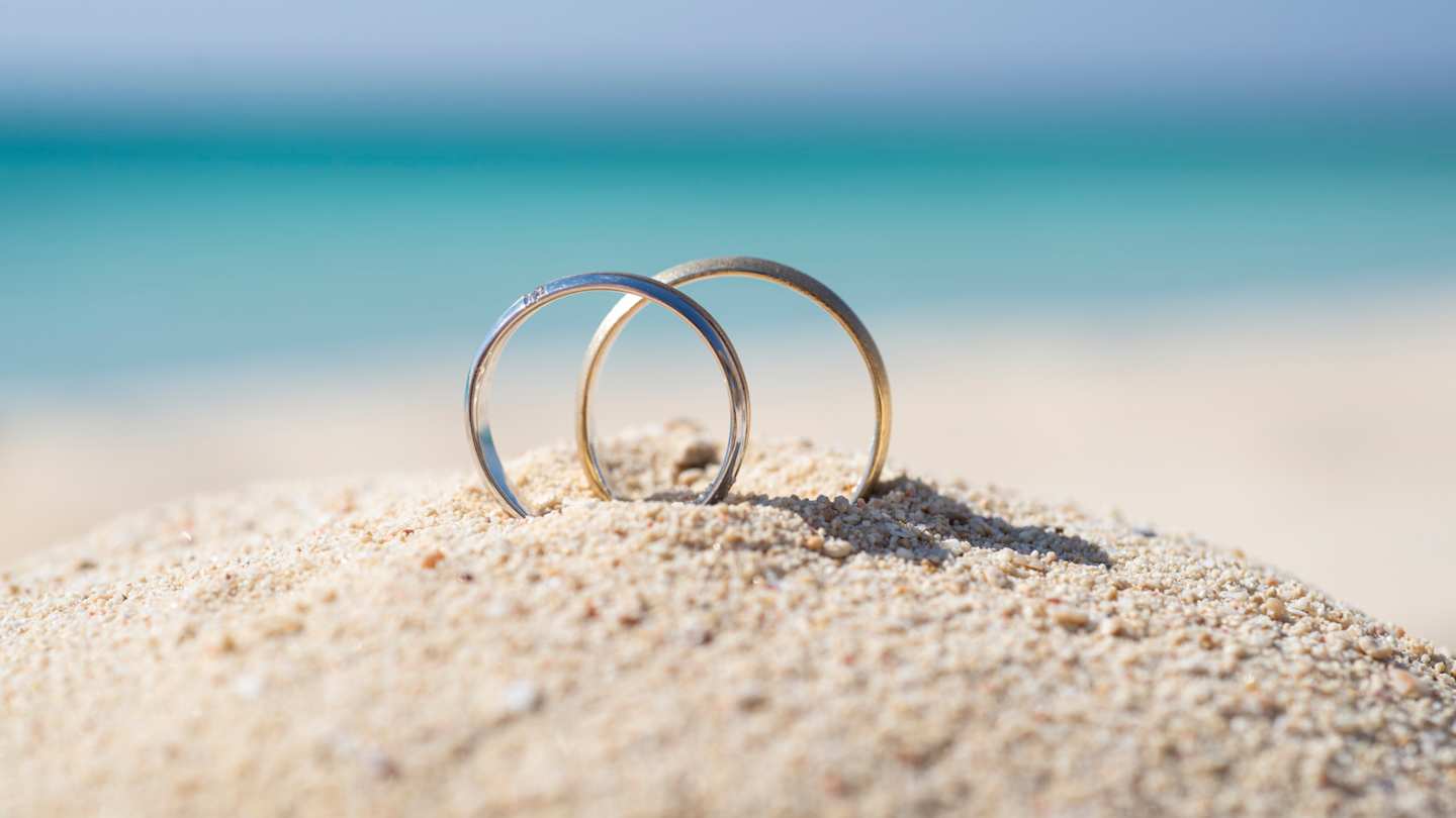 A close up view of two rings in a pile of sand at a beach on a honeymoon