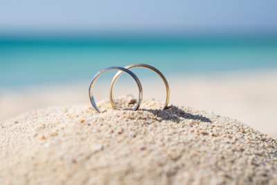 A close up view of two rings in a pile of sand at a beach on a honeymoon