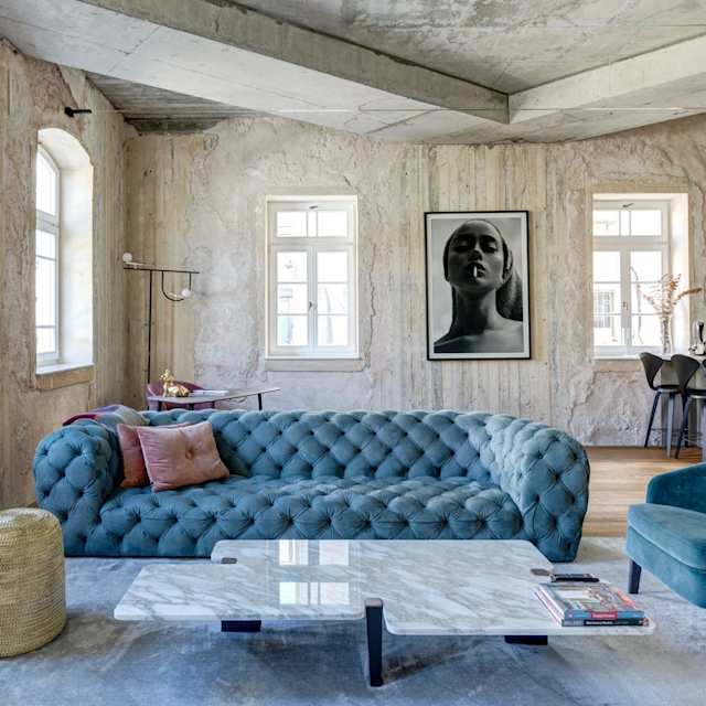 Blue sofa and exposed concrete wall in living room of Plum Guide home, Concrete Heritage