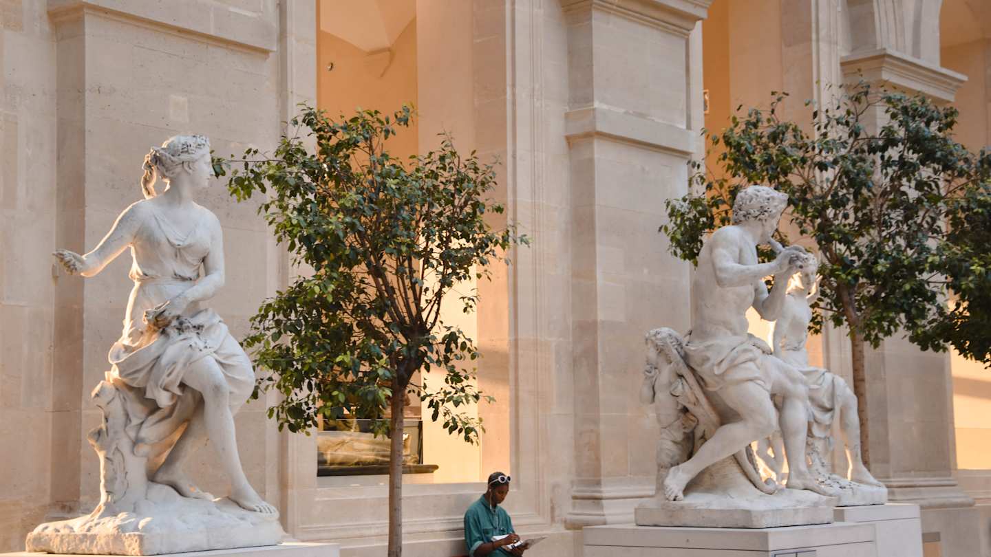 Person sat down in between two sculptures in the Louvre, Paris