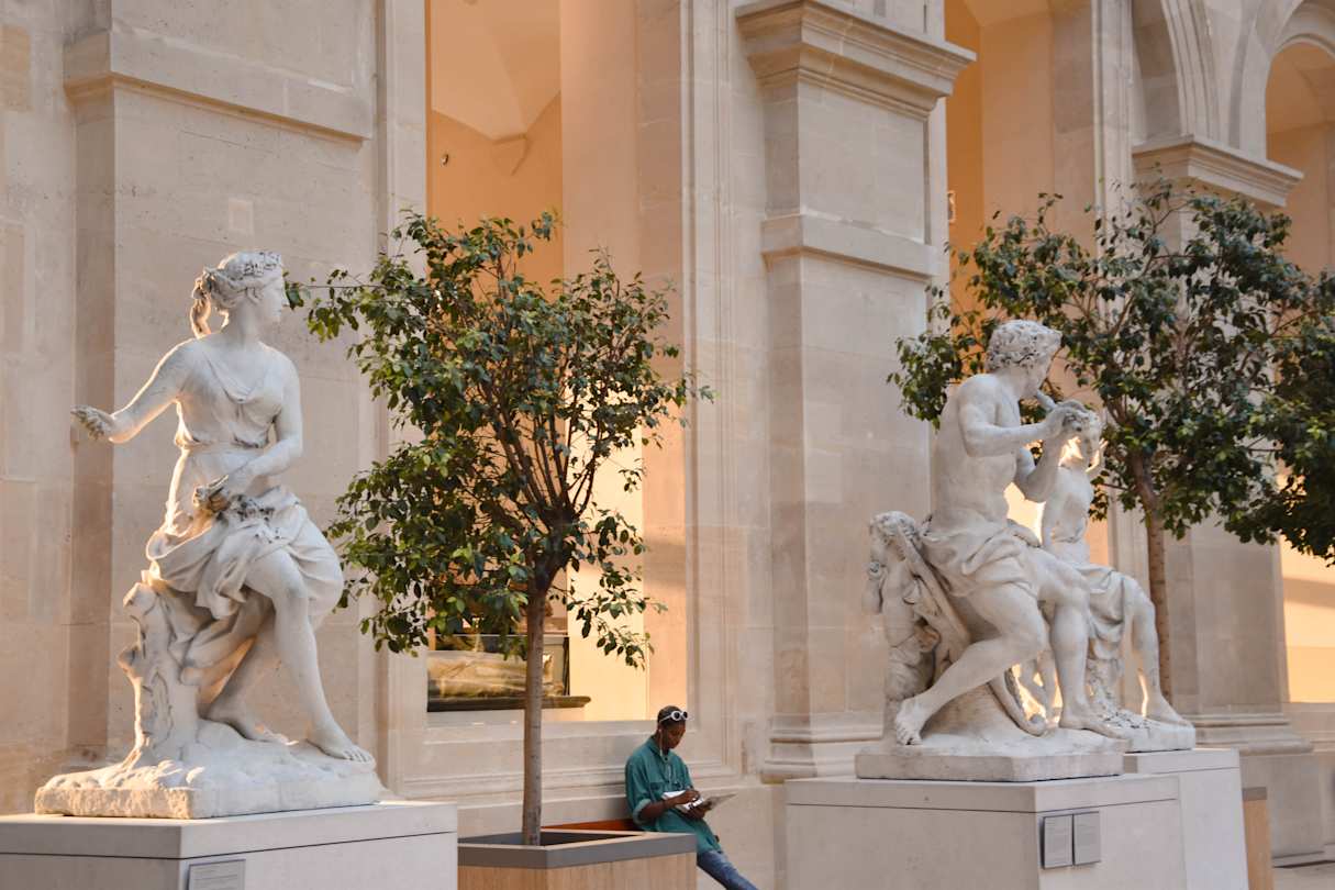 Person sat down in between two sculptures in the Louvre, Paris
