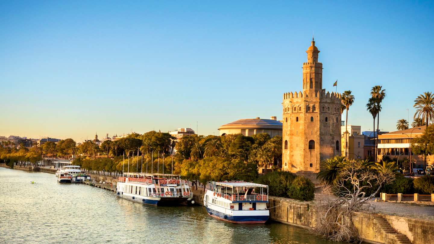 View of Golden Tower (Torre del Oro) and boats on the River Guadalquivir at sunset, Seville