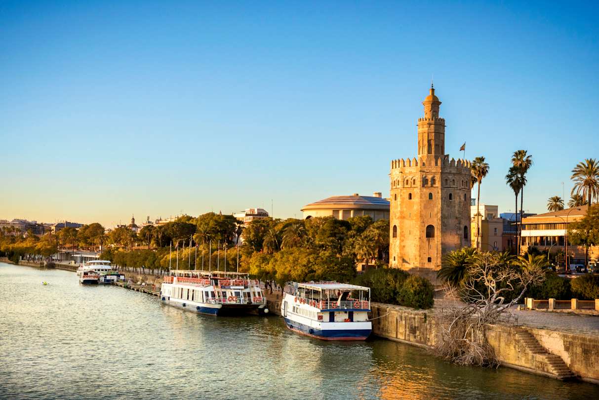 View of Golden Tower (Torre del Oro) and boats on the River Guadalquivir at sunset, Seville