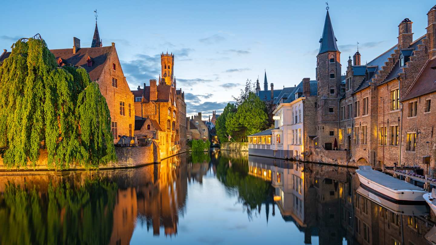 A view of a small canoes on a canal by brick buildings at sunset, Bruges, Belgium