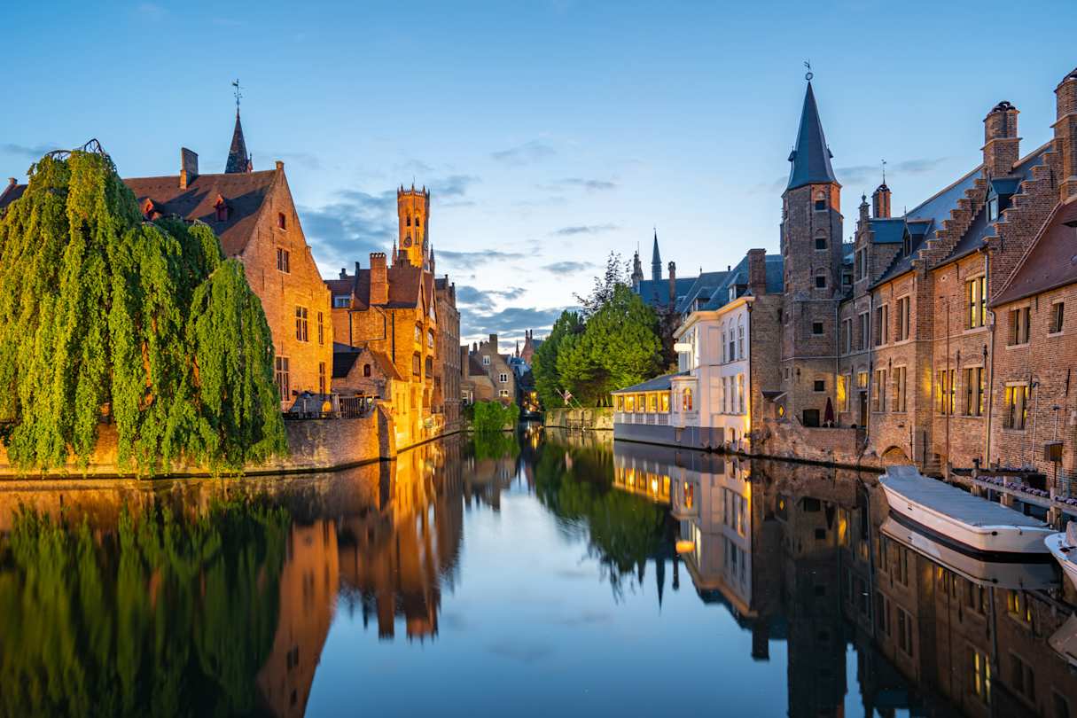A view of a small canoes on a canal by brick buildings at sunset, Bruges, Belgium