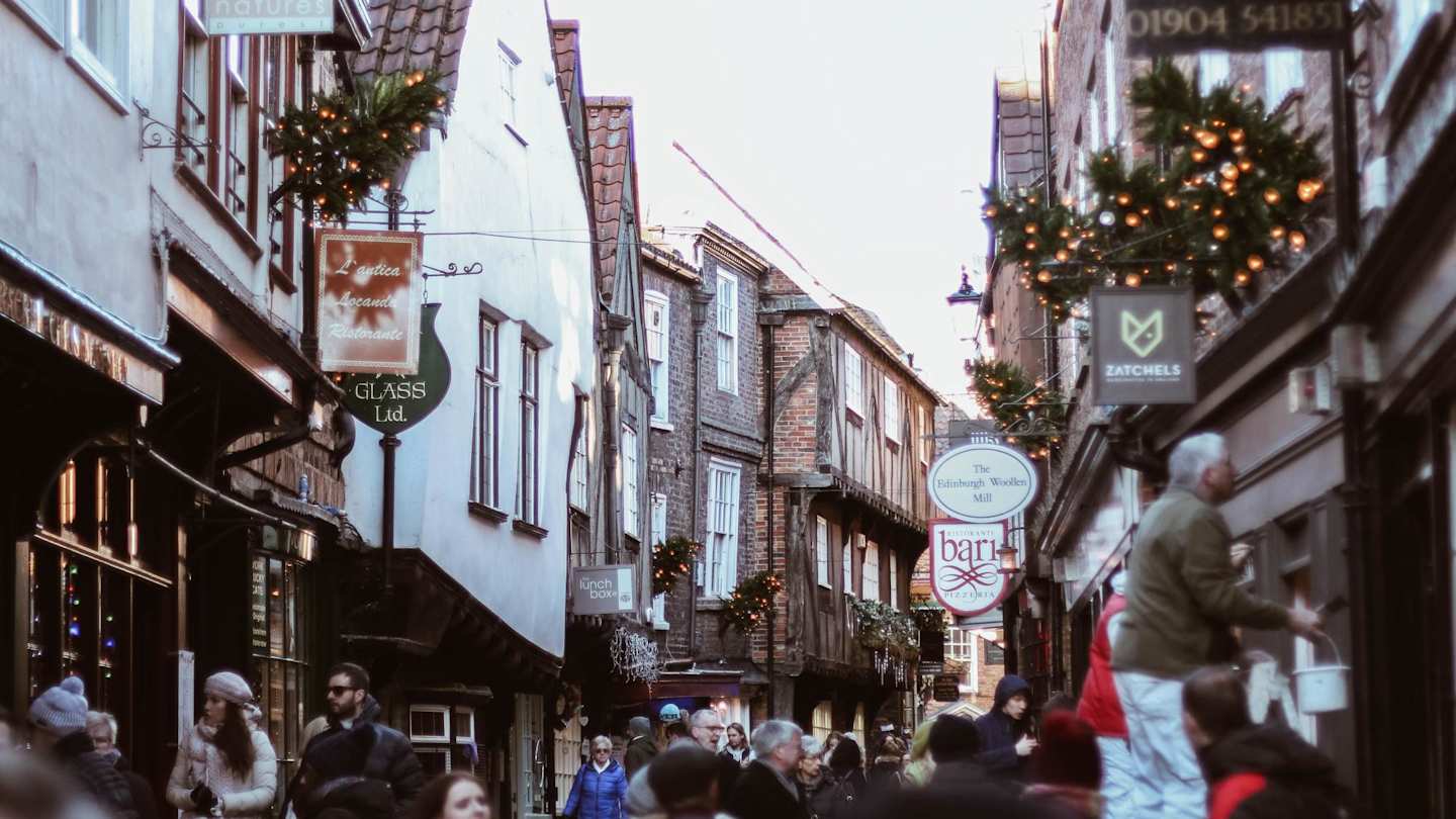 People walking along The Shambles in front of shops in York, England, UK