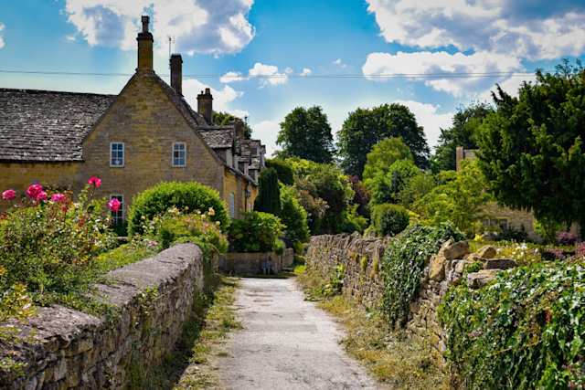 A country lane by cottages and green plants in the Cotswolds, England, UK