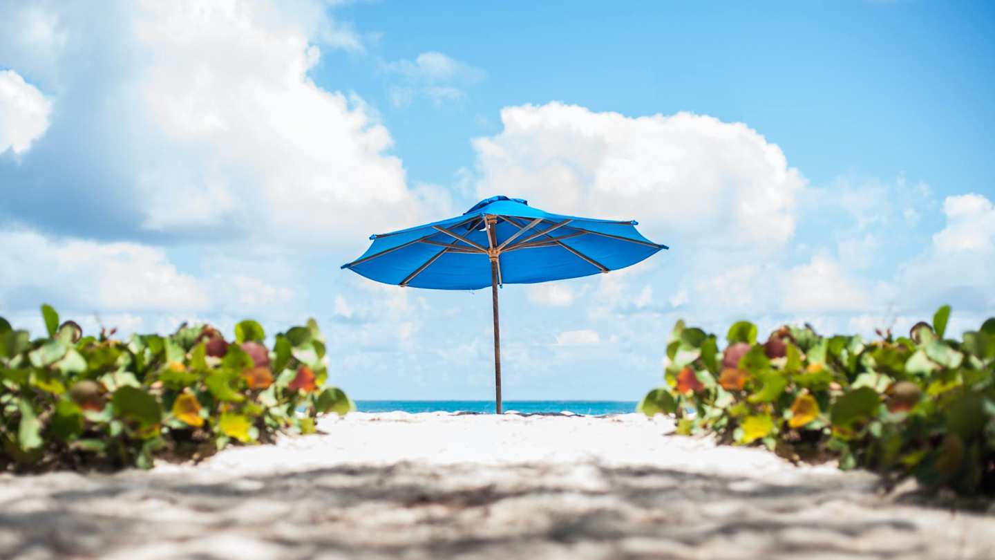 A blue parasol on the beach in Barbados in front of the blue sea