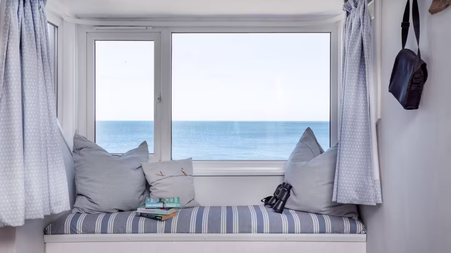 Window seat with blue striped cushions, a small stack of books, and pair of binoculars, sea views in the background, Devon
