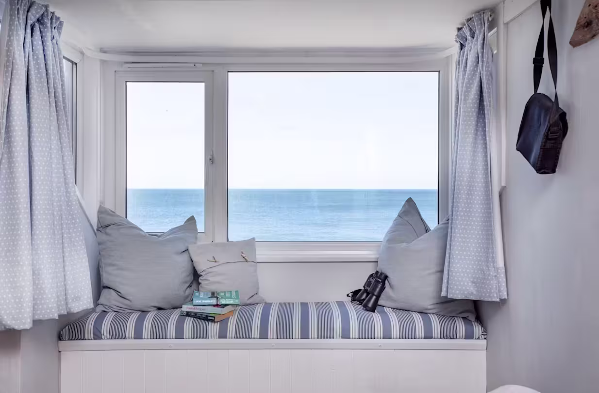 Window seat with blue striped cushions, a small stack of books, and pair of binoculars, sea views in the background, Devon
