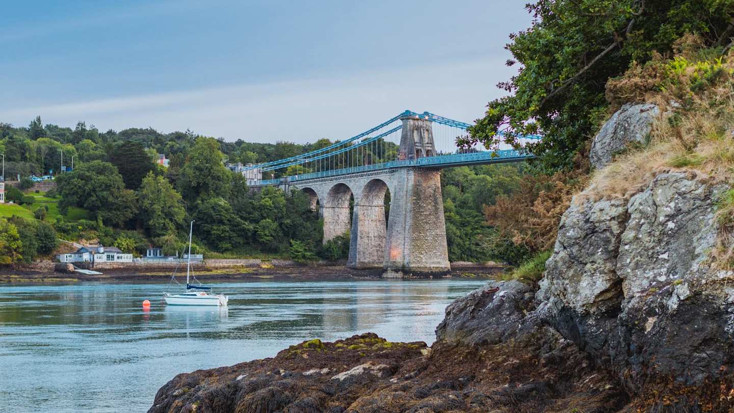 A bridge and a body of water next to some rocks in Menai Bridge, Anglesey, Wales, UK