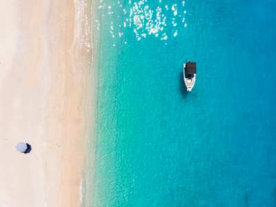 A bird's eye view of one parasol on the sand and a small boat in the clear blue sea at a beach in Kefalonia, Greece