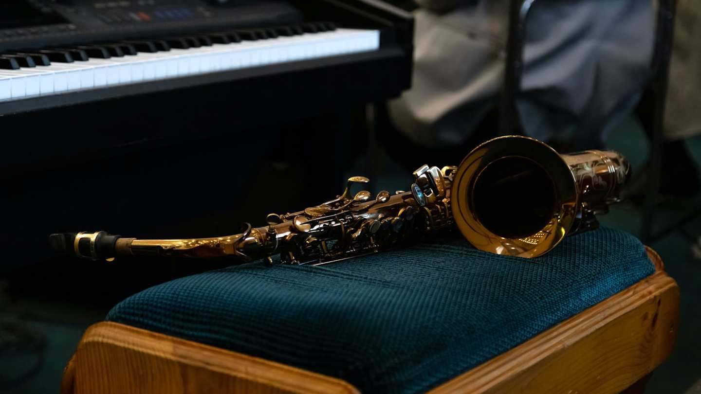 Gold saxaphone lying on a soft stool next to a piano