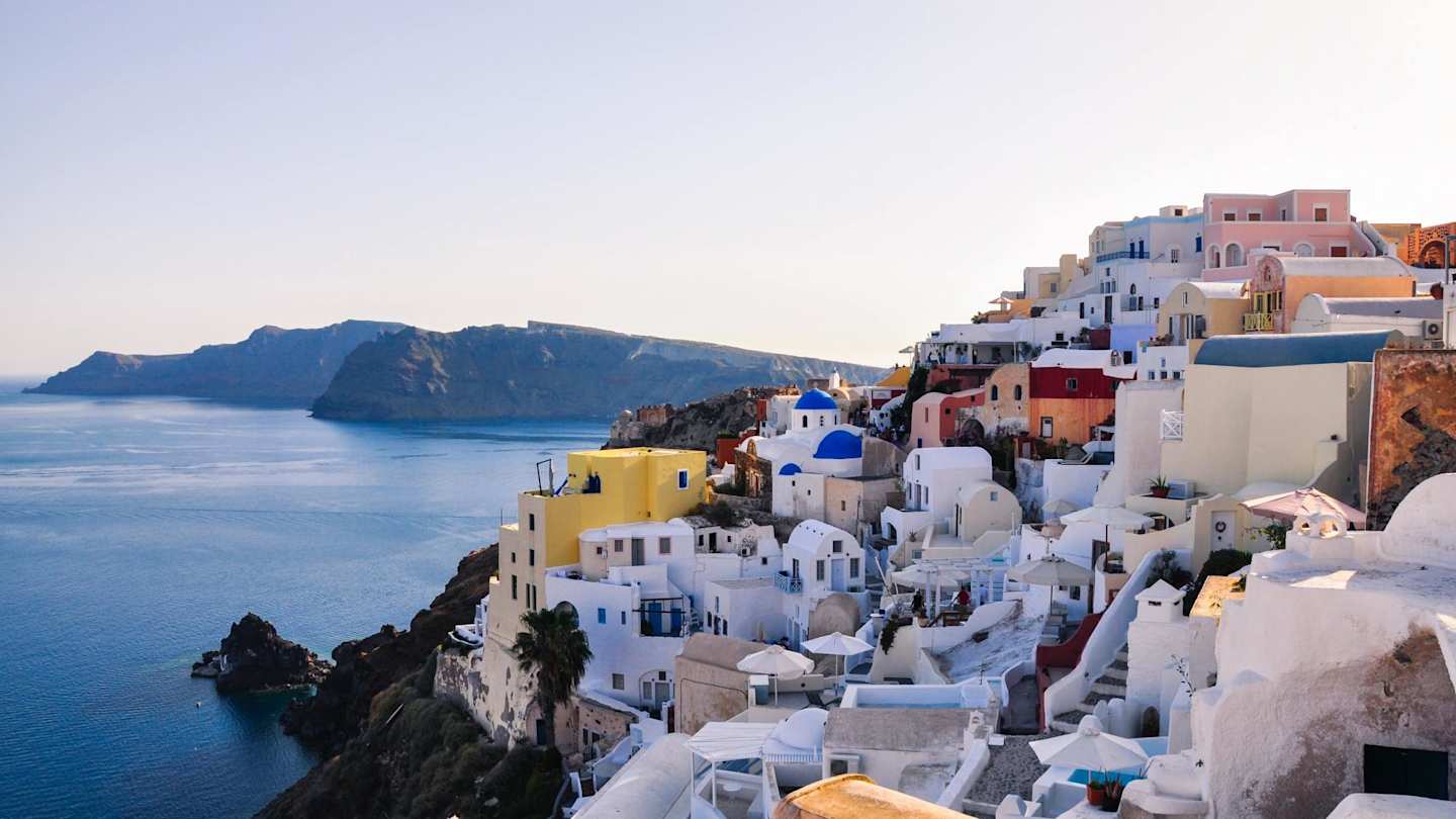 Numerous white buildings sitting on the side of a mountain overlooking the sea in Santorini, Greece